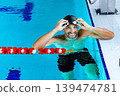 Portrait of a positive professional swimmer in a pool wearing swimming goggles, resting after swimming in the pool 139474781