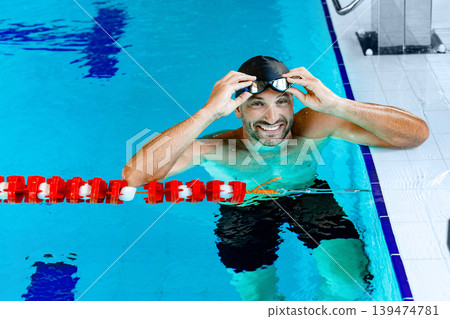 Portrait of a positive professional swimmer in a pool wearing swimming goggles, resting after swimming in the pool Portrait of a positive professional swimmer in a pool wearing swimming goggles, resting after swimming in the pool 139474781