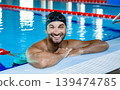 Positive swimmer, wearing swim goggles and swimming cap, relaxing in the pool after training. 139474785