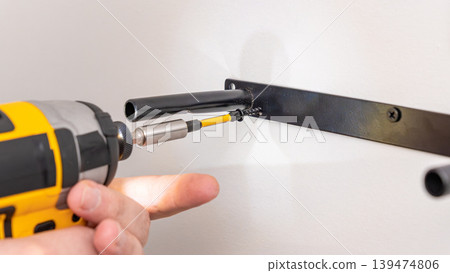 Mans hands using yellow cordless drill with extension to fasten screw into wall bracket. Home improvement, installing support, DIY extension use, precise fastening. Mans hands using yellow cordless drill with extension to fasten screw into wall bracket. Home improvement, installing support, DIY extension use, precise fastening. 139474806