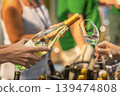 White wine tasting at indoor event with bottle and glass close-up. Wine being poured from glass bottle into tasting glass, blurred people, bottles, warm lights, shallow depth of field in background 139474808