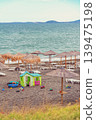 Empty sun loungers and colorful toys scattered on black sand beach with straw umbrellas at quiet seashore. Concept of end summer, vacation nostalgia, off-season solitude 139475198