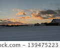Peaceful winter countryside with snowy fields village houses and dramatic sunset clouds. Cold seasonal landscape with warm evening light and rural atmosphere 139475223