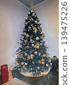 Elegant Christmas tree decorated with golden ornaments and glowing fairy lights in a cozy modern interior. Warm winter holiday atmosphere with classic seasonal decor 139475226