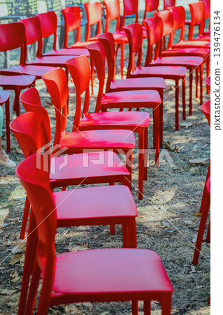 Rows of red chairs arranged outdoors for event, chairs prepared for audience, meeting, seminar, ceremony, presentation, festival. Concept of chair seating, organization, gathering, public ceremony Rows of red chairs arranged outdoors for event, chairs prepared for audience, meeting, seminar, ceremony, presentation, festival. Concept of chair seating, organization, gathering, public ceremony 139476134