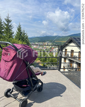 Toddler in a Stroller on a Terrace with Bukovel Mountain View Toddler in a Stroller on a Terrace with Bukovel Mountain View 139476252
