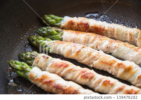 Meat-wrapped asparagus cooked in a frying pan 139476282