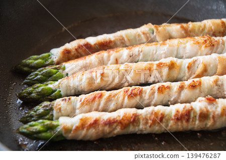 Meat-wrapped asparagus cooked in a frying pan 139476287