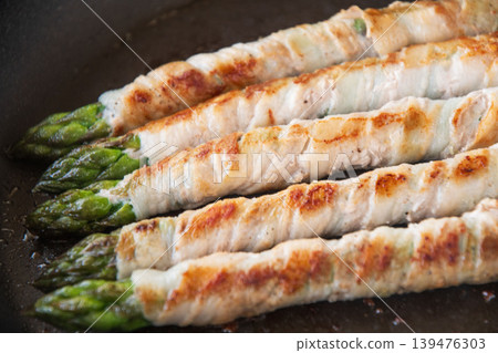 Meat-wrapped asparagus cooked in a frying pan Meat-wrapped asparagus cooked in a frying pan 139476303