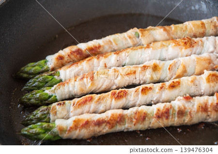 Meat-wrapped asparagus cooked in a frying pan Meat-wrapped asparagus cooked in a frying pan 139476304