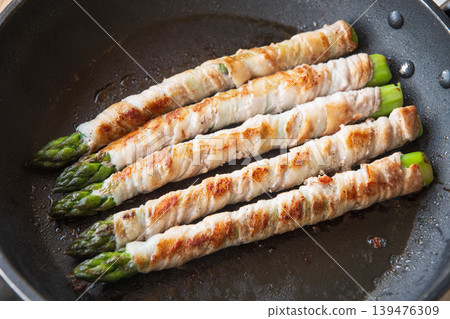 Meat-wrapped asparagus cooked in a frying pan Meat-wrapped asparagus cooked in a frying pan 139476309