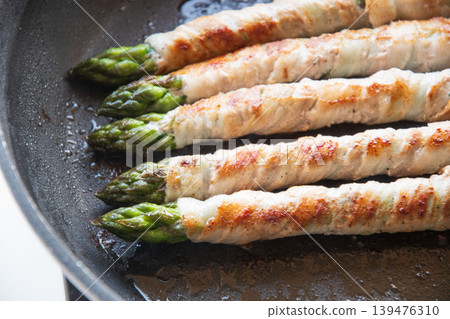 Meat-wrapped asparagus cooked in a frying pan Meat-wrapped asparagus cooked in a frying pan 139476310