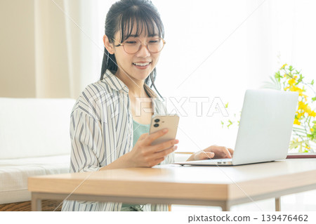 A young woman using a computer and a smartphone 139476462