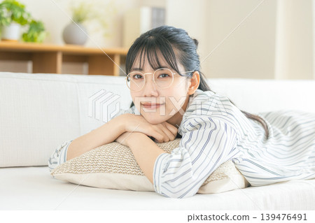 一位戴眼鏡的年輕女子躺在客廳放鬆。 139476491
