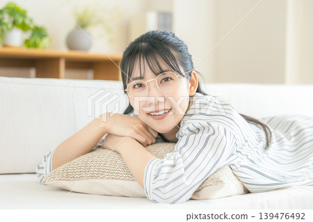 一位戴眼鏡的年輕女子躺在客廳放鬆。 139476492