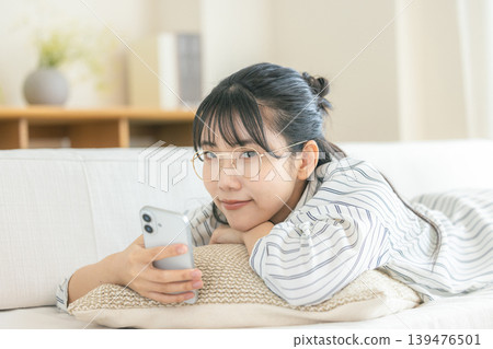 一位戴眼鏡的女子躺著看著她的智慧型手機。 一位戴眼鏡的女子躺著看著她的智慧型手機。 139476501