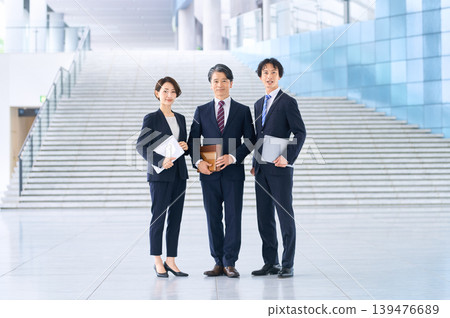 A business team of three: Japanese businessmen and businesswomen, smiling, standing side-by-side in front of the stairs. A business team of three: Japanese businessmen and businesswomen, smiling, standing side-by-side in front of the stairs. 139476689