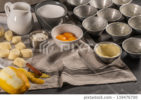 Ingredients for homemade baking portuguese egg tarts - flour, milk, water, egg, sugar, lemon, cinnamon, pastry and cake pan. Traditional portuguese dessert pastel de nata 139476780