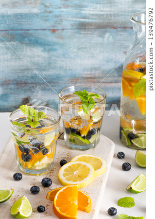Summer healthy cocktails of citrus infused waters, lemonades or mojitos, with lime lemon orange blueberries and mint, diet detox beverages, in glasses on light background Summer healthy cocktails of citrus infused waters, lemonades or mojitos, with lime lemon orange blueberries and mint, diet detox beverages, in glasses on light background 139476792