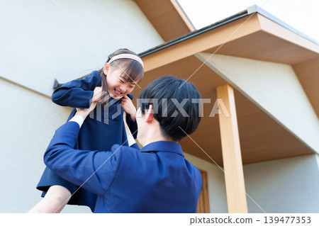 A father lifts his daughter up in front of his house. A father lifts his daughter up in front of his house. 139477353