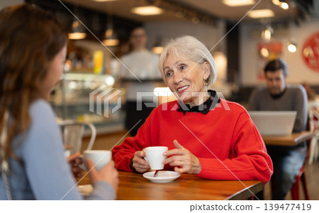 Elderly woman meets her adult daughter in cafe. Conversation over cup of coffee Elderly woman meets her adult daughter in cafe. Conversation over cup of coffee 139477419