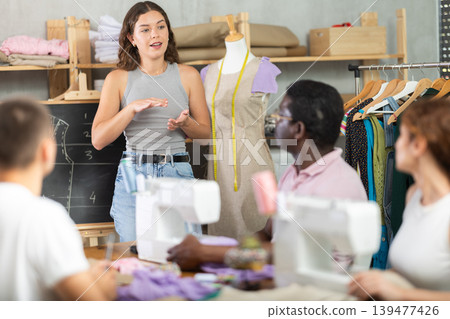 Sewing school girl teacher conducts lesson for students using mannequin Sewing school girl teacher conducts lesson for students using mannequin 139477426