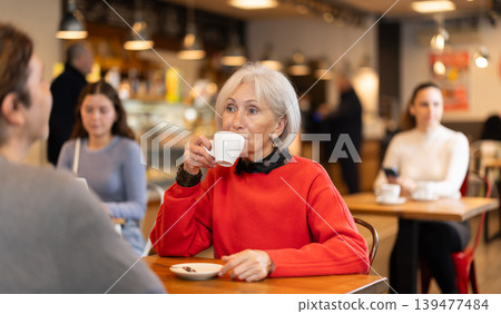 Senior woman in cafe sits opposite male companion, has nice conversation Senior woman in cafe sits opposite male companion, has nice conversation 139477484