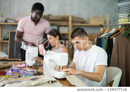 Interested guy working at machine during group sewing course for adults Interested guy working at machine during group sewing course for adults 139477536