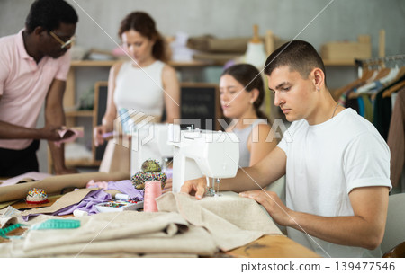 Engaged guy stitching fabric on machine in sewing class for adults Engaged guy stitching fabric on machine in sewing class for adults 139477546