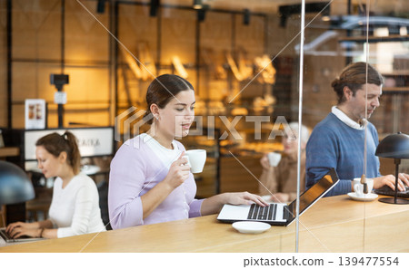 Smiling woman using laptop and drinking coffee in modern cafe 139477554