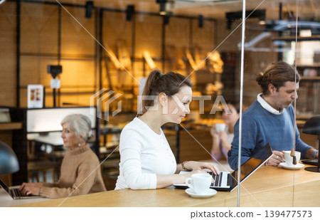 Interested female designer sitting in cafe with coffee and laptop Interested female designer sitting in cafe with coffee and laptop 139477573