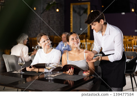 Waiter guy tells young women visitors of cafe about dish from chef Waiter guy tells young women visitors of cafe about dish from chef 139477584