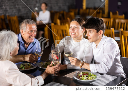 Young family and elderly couple of spouses eating in cafe celebrating event and communicating 139477612