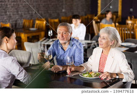 Elderly couple with adult woman having dinner in restaurant Elderly couple with adult woman having dinner in restaurant 139477618