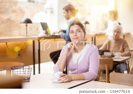 Dreamy young girl drinking coffee in cozy cafe Dreamy young girl drinking coffee in cozy cafe 139477619