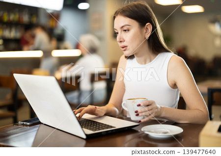 Young woman with laptop drinking coffee Young woman with laptop drinking coffee 139477640