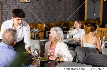 Restaurateur guy serves customers elderly spouses plate with dinner order Restaurateur guy serves customers elderly spouses plate with dinner order 139477644