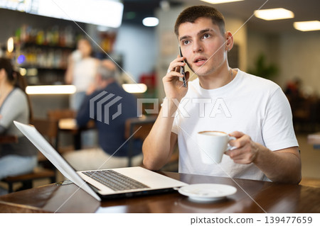 Guy working on laptop and answering call Guy working on laptop and answering call 139477659