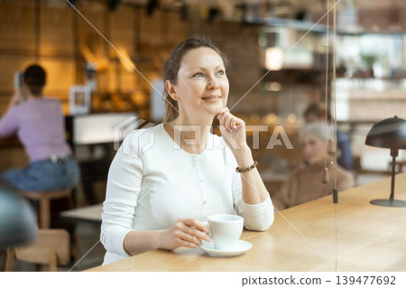 Relaxed woman sitting alone drinking coffee in quiet cafe Relaxed woman sitting alone drinking coffee in quiet cafe 139477692