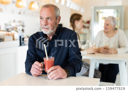 Senior man visitor sits near table, drink juice in chain cafe shop Senior man visitor sits near table, drink juice in chain cafe shop 139477819
