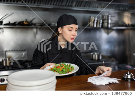 Woman cook checks paid check and cooked dish in kitchen Woman cook checks paid check and cooked dish in kitchen 139477900