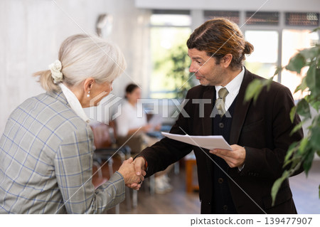 Adult man and elderly woman shaking hands in office Adult man and elderly woman shaking hands in office 139477907