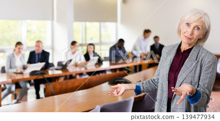 Elegant senior white businesswoman posing with welcoming hand gesture Elegant senior white businesswoman posing with welcoming hand gesture 139477934