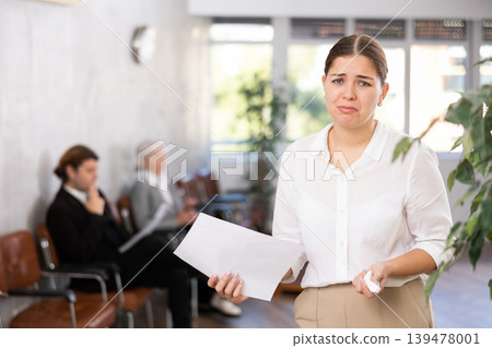 Portrait of upset disappointed female office employee holding paper document in hands Portrait of upset disappointed female office employee holding paper document in hands 139478001