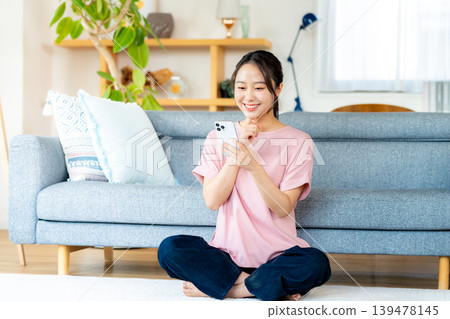 在房間裡操作智慧型手機的年輕女子 在房間裡操作智慧型手機的年輕女子 139478145