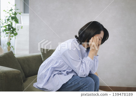一位四十多歲的女子坐在沙發上，雙手抱頭。 139478189