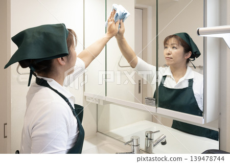 A house cleaning lady wiping the bathroom mirror. A house cleaning lady wiping the bathroom mirror. 139478744