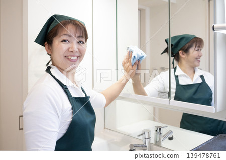 A house cleaning lady wiping the bathroom mirror. A house cleaning lady wiping the bathroom mirror. 139478761