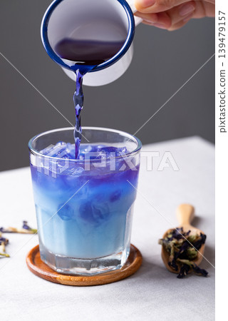 Pouring butterfly pea tea into a glass with iced and milk to make a healthy cold drink for summer Pouring butterfly pea tea into a glass with iced and milk to make a healthy cold drink for summer 139479157