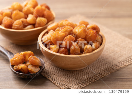 Dried longan in a wooden bowl with spoon on a wooden background Dried longan in a wooden bowl with spoon on a wooden background 139479169